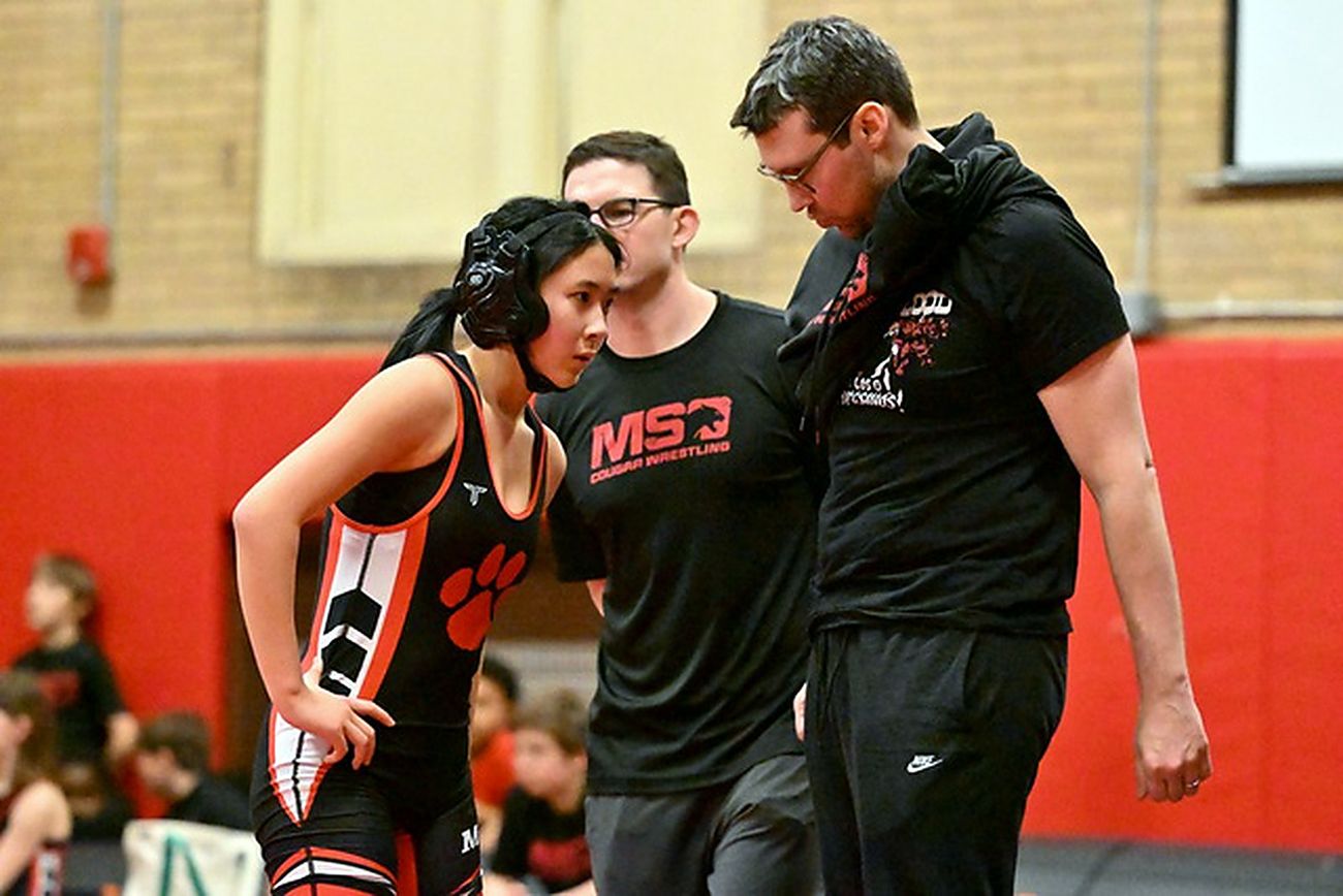 Two MSO coaches talking with a wrestler at the edge of the mat.