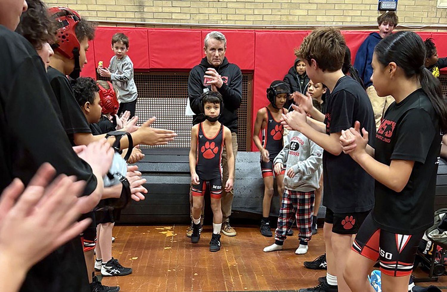 MSO teammates lining up and clapping a young wrestler onto the mat.